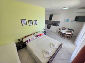 Hotellihuone, jossa on sänky, pieni työpöytä, tuoli, pieni keittiö ja ruokapöytä.