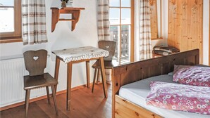 Ein gemütliches Zimmer mit einem hölzernen Bett, einem kleinen Tisch mit Spitze, zwei Stühlen und einem Schrank mit Haken.