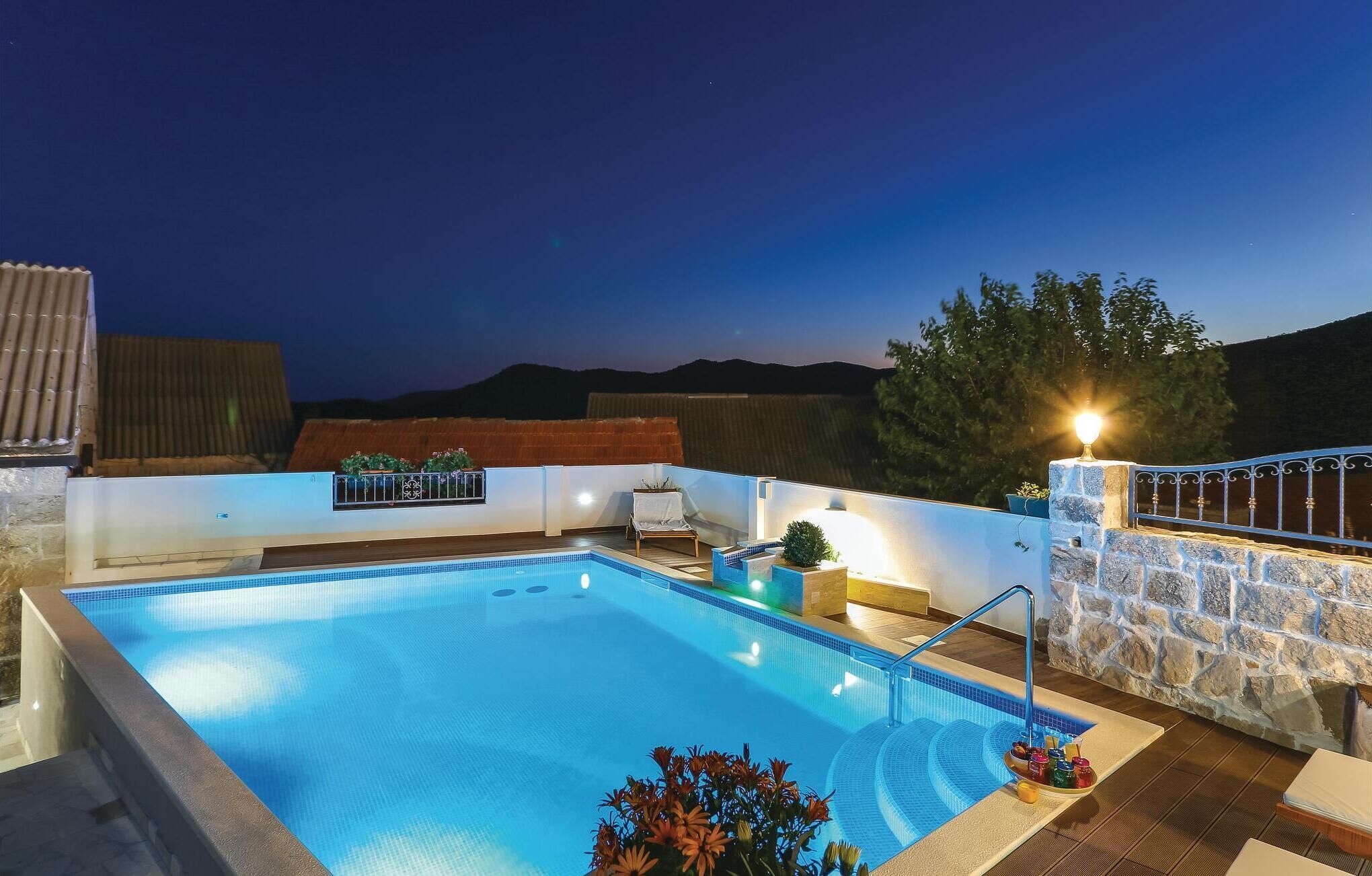 Une piscine avec un mur en pierre et une rambarde en métal. On y trouve une chaise et une petite table avec une plante.