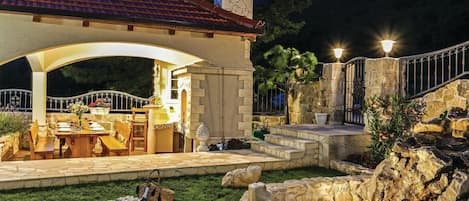 A patio area with a dining table set for two, a stone fountain, and a stone wall with a gate.