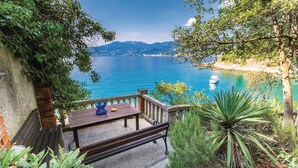 A wooden deck with a table and bench overlooking a body of water with boats, surrounded by greenery and mountains in the background. - Cozy apartment in Rijeka with WiFi (Rijeka)