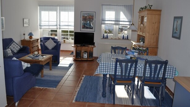 A living room with a sofa, a coffee table, a television, and a dining area with a table and chairs. - FeWo Möwennest / Felstehausen GM 69252 - FeWo Möwennest (Graal-Müritz)