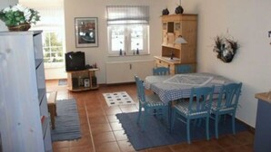 A compact living space with a dining area, kitchenette, and a window with curtains. - FeWo Möwennest / Felstehausen GM 69252 - FeWo Möwennest (Graal-Müritz)
