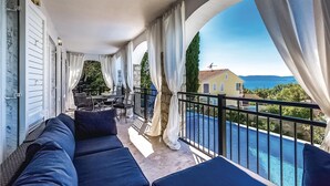 Un balcon avec vue sur la piscine, un espace salon extérieur et un mur en pierre.