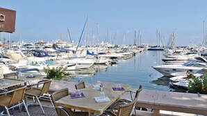 Marina com vários barcos atracados. Há mesas e cadeiras ao ar livre, com copos vazios e guardanapos.