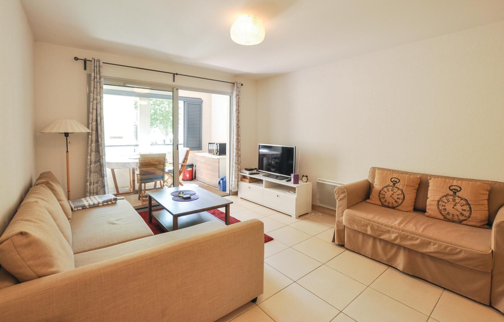 A living room with a sofa, a coffee table, a TV on a stand, and a lamp. There is a sliding glass door leading to an outdoor area.