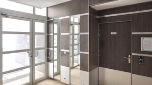 Quarto de hotel moderno com uma ampla porta de vidro deslizante que dá para uma varanda, uma porta separada com espelho e uma placa indicando acesso às garagens.