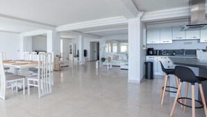 Un vaste espace de vie comprenant un coin repas avec table et chaises, une cuisine équipée d’appareils modernes et une grande fenêtre laissant entrer la lumière naturelle.