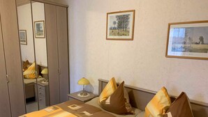 Una camera d'albergo con un letto, un comodino, una lampada, un armadio e due quadri appesi al muro.