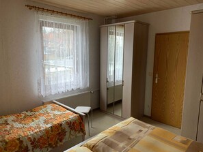 A bedroom with a single bed, a small table, a wardrobe, and a window with a curtain. - FW 2 (in the house) - Apartments Rießling (Elend)