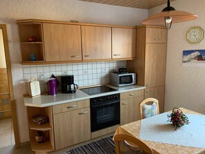 A kitchen with wooden cabinets, a microwave, a coffee maker, and a table with a lace tablecloth. - FW 2 (in the house) - Apartments Rießling (Elend)