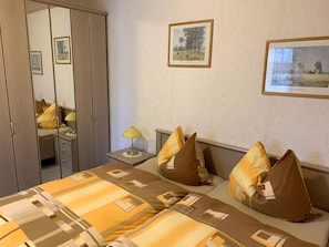 A hotel room with a bed, a nightstand, a lamp, a wardrobe, and two framed pictures on the wall. - FW 2 (in the house) - Apartments Rießling (Elend)
