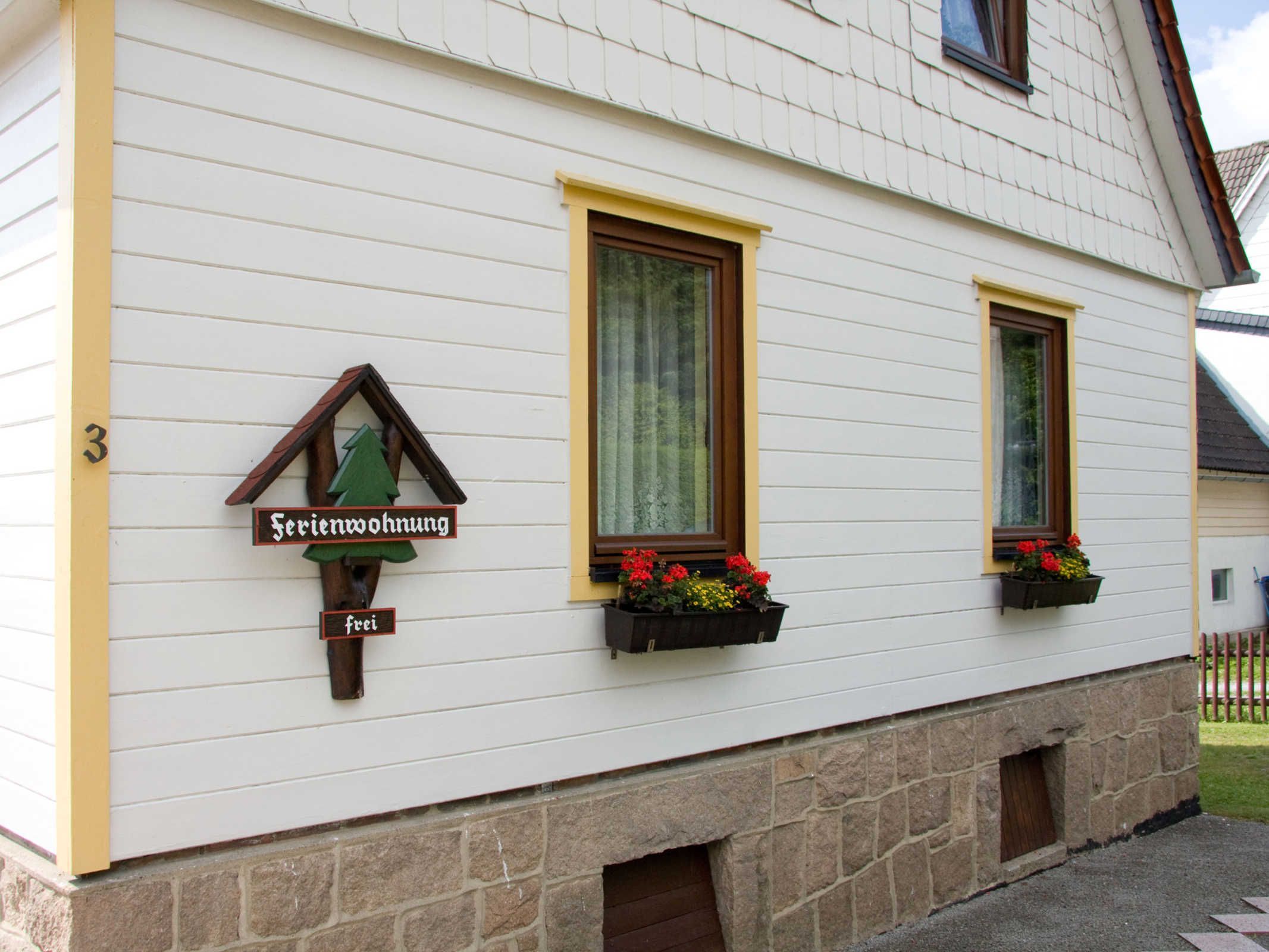 Un edificio blanco con un letrero de madera que dice 'Serenwohnung frei' y dos ventanas adornadas con macetas de flores.