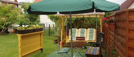 Un jardín con un columpio, un banco y una mesa bajo un paraguas verde.