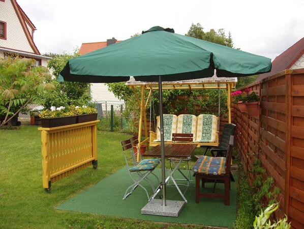 A garden with a swing set, a bench, and a table under a green umbrella. - FW 2 (in the house) - Apartments Rießling (Elend)