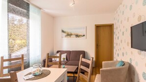 Un salon confortable avec un canapé, une table à manger et des chaises, un téléviseur fixé au mur et une porte donnant sur une autre pièce.