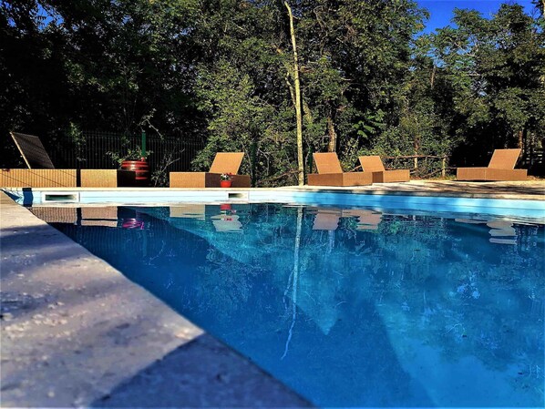 A swimming pool with lounge chairs and a fenced area, surrounded by trees.