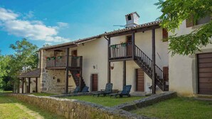 A two-story building with a stone facade, a wooden balcony, and a staircase leading to the upper floor. There are lounge chairs on the ground floor. - Holiday home in a quiet location for nature lovers (Buzet)
