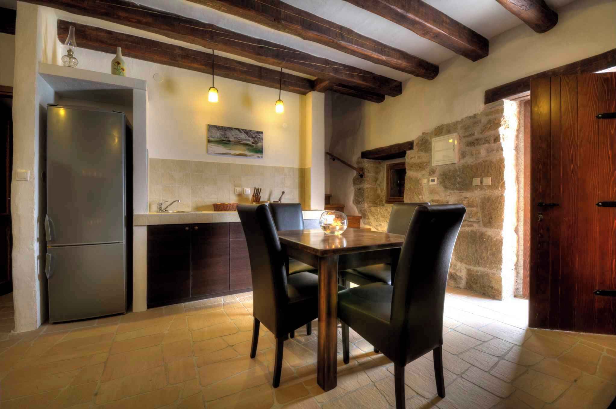 A kitchen with a wooden table and chairs, a refrigerator, and a stone wall.