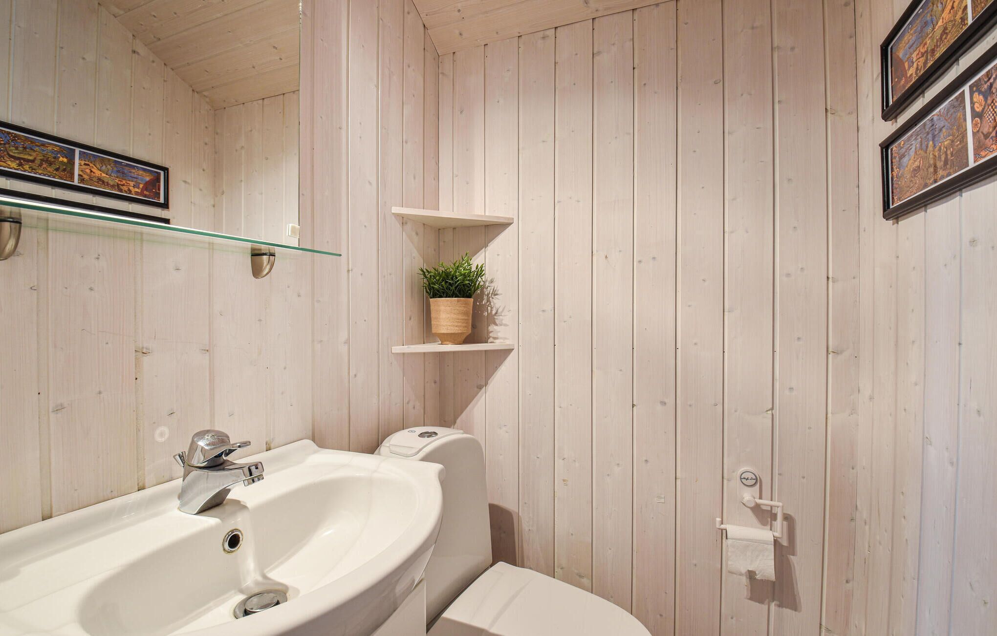 A bathroom with wooden panel walls, a glass shelf with a plant, and a toilet with a paper towel holder.