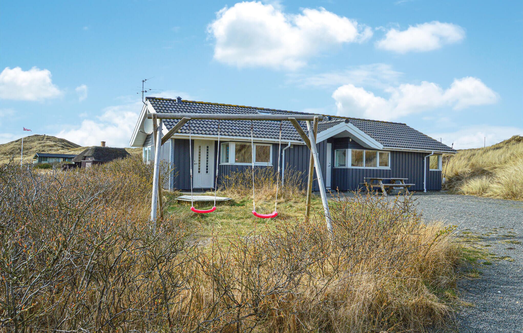 A coastal house with a thatched roof, a swing set, and a picnic table.