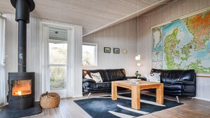 Un salon chaleureux avec un poêle à bois, un canapé en cuir, une table basse en bois et une grande carte du Danemark accrochée au mur.