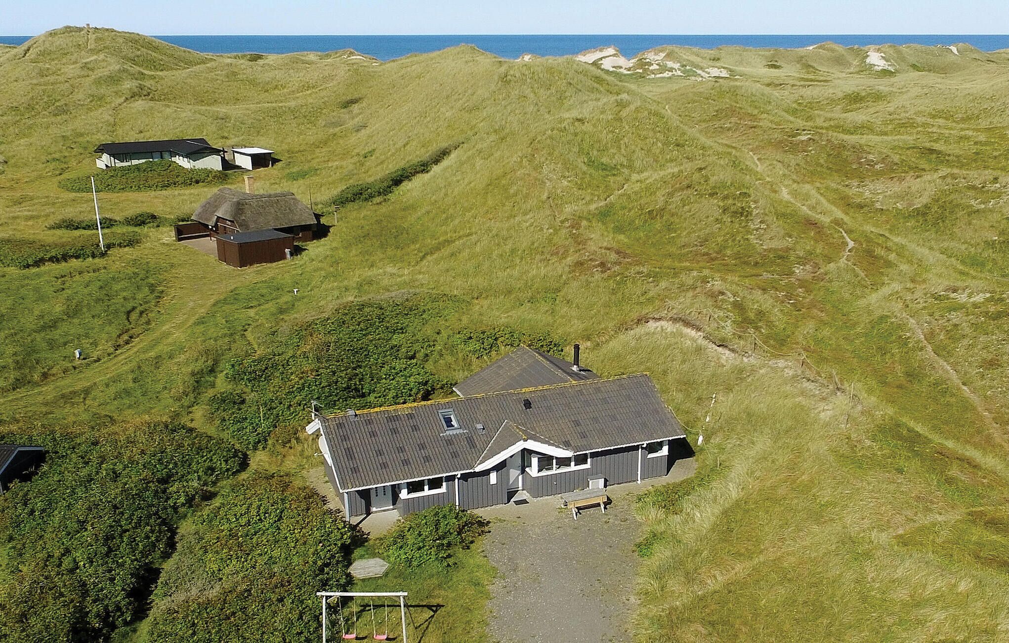 Une maison avec un toit en pente, entourée de collines verdoyantes et sous un ciel dégagé.