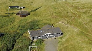Une maison avec un toit en pente, entourée de collines verdoyantes et sous un ciel dégagé.