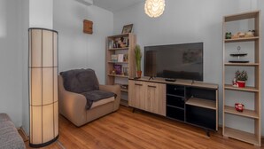 Een moderne woonkamer met een bank, televisie, houten planken en een vloerlamp.