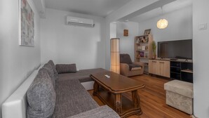 Een moderne woonkamer met een hoekbank, een houten salontafel, een boekenkast, een televisie en een vloerlamp.