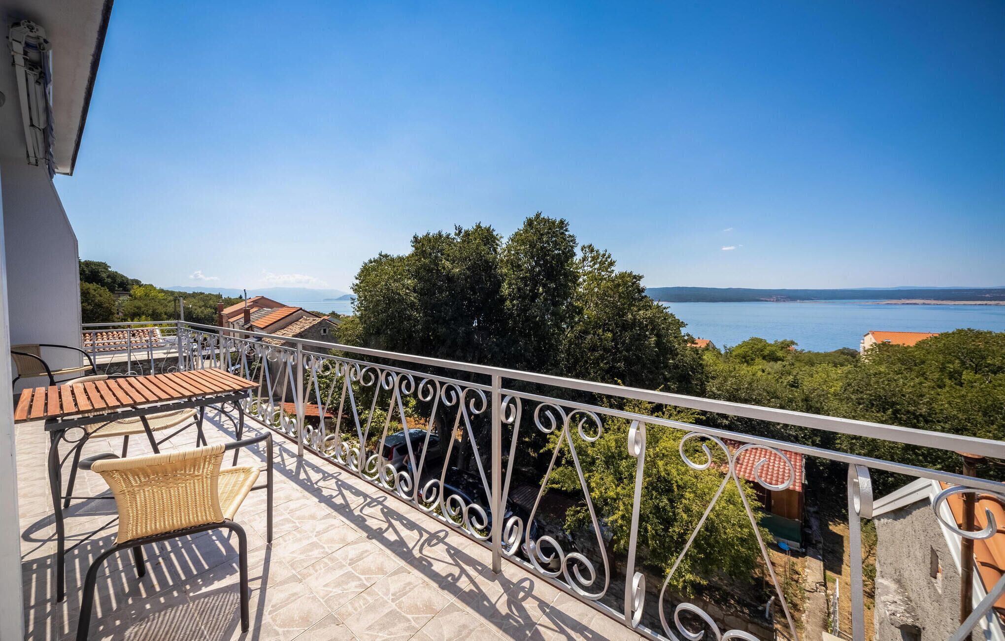 Ein Balkon mit Meerblick, ein Korbstuhl und ein Tisch.