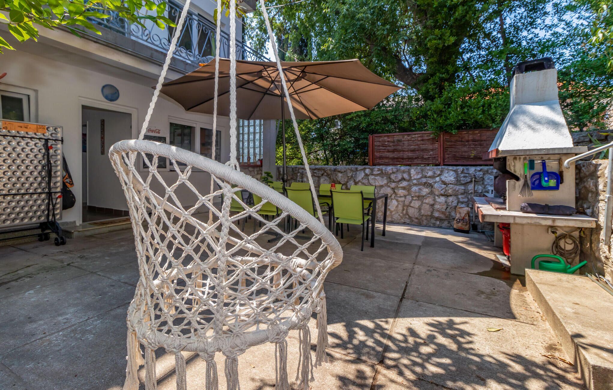 Un espace patio aménagé avec un fauteuil suspendu, des sièges d’extérieur, un barbecue et un mur en pierre.