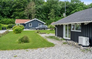 A house with a gravel driveway, a car parked in the driveway, and a small garden area with a hedge and a bush.