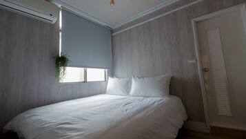 Un dormitorio con una cama, una ventana con persianas, una planta colgante y una puerta.