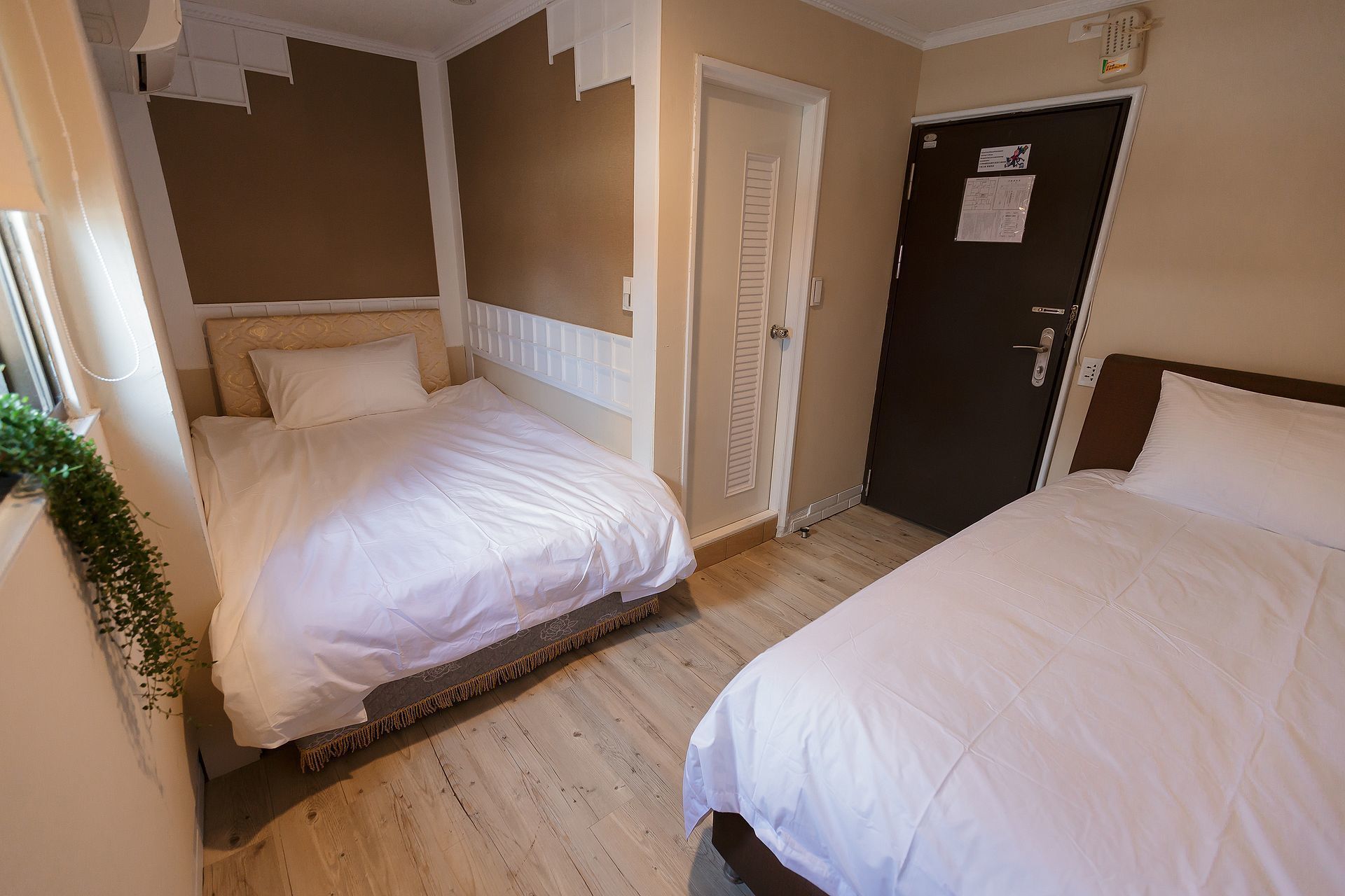 A hotel room with two beds, a door, and a small window.