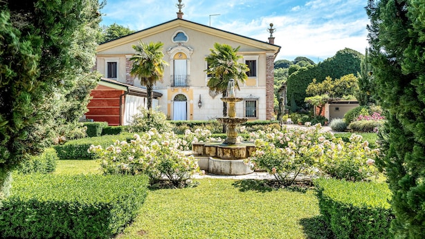 Un bâtiment historique doté d’une fontaine centrale, entouré de jardins et de haies bien entretenus.