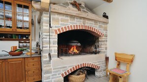 Een keuken met een stenen openhaard, houten kastjes en een geweven mand onder de haard.