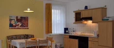 A compact kitchen with wooden cabinets, a dining table with chairs, and a pendant light.