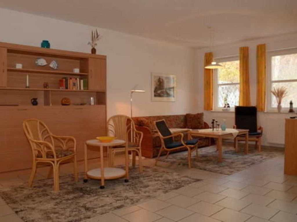 Un salon comprenant un canapé, des fauteuils, une table basse, une bibliothèque, un tableau et une fenêtre avec des rideaux.