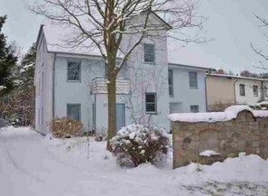 Un edificio de dos pisos con una entrada de pared de piedra, techo cubierto de nieve y un ventanal visible.