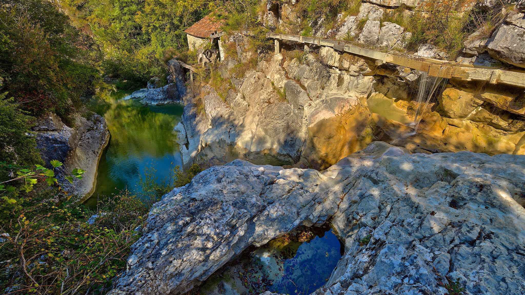 Formación rocosa natural con una cascada pequeña y un puente de madera.