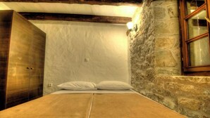A bedroom with a bed, white pillows, a wooden wardrobe, and a stone wall. - Holiday home in a quiet location and with barbecue (Buzet)