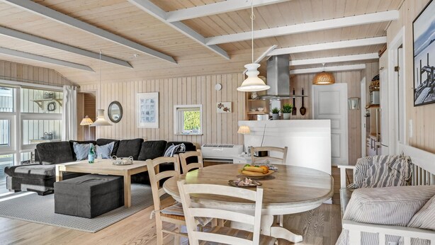 A spacious living area with a wooden dining table, a sofa, and a kitchen in the background. - 3 bedroom lovely home in Melby (Melby)