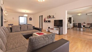 A modern living room with a large sofa, a TV, and a dining area with chairs and a table. - Awesome home in Frkeci (Frkeci)