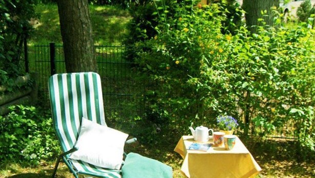 Ein grün-weißer Streifenloungesessel mit Kissen, ein kleiner Tisch mit gelber Tischdecke und ein Buch.