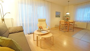 Ein modernes Wohnzimmer mit einer Couch, einem Esstisch mit Stühlen, einem Sessel und einer Lampe.