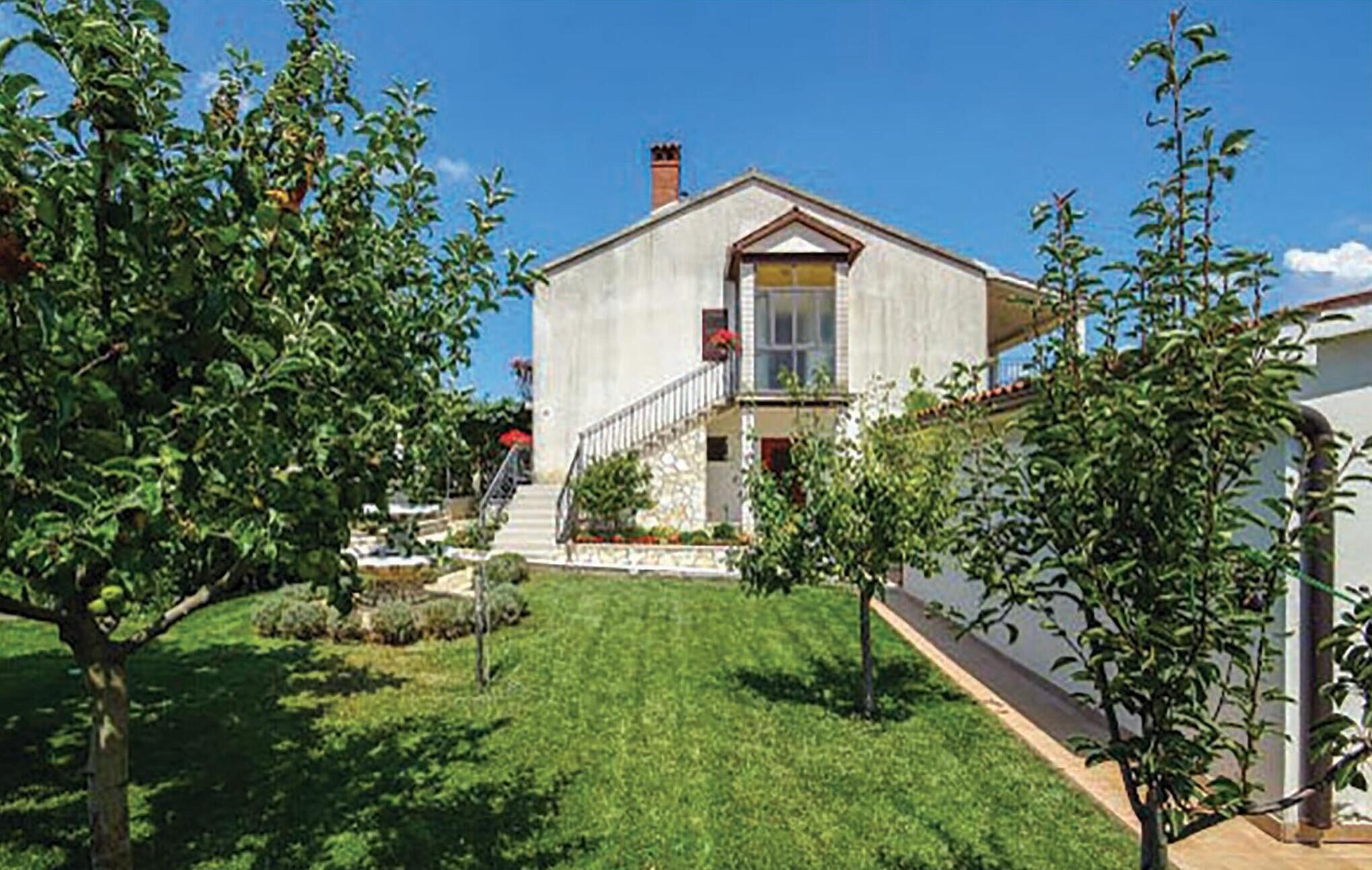 A two-story house with a front yard, a staircase leading to the entrance, and a small garden area.