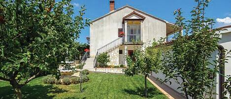 A two-story house with a front yard, a staircase leading to the entrance, and a small garden area.
