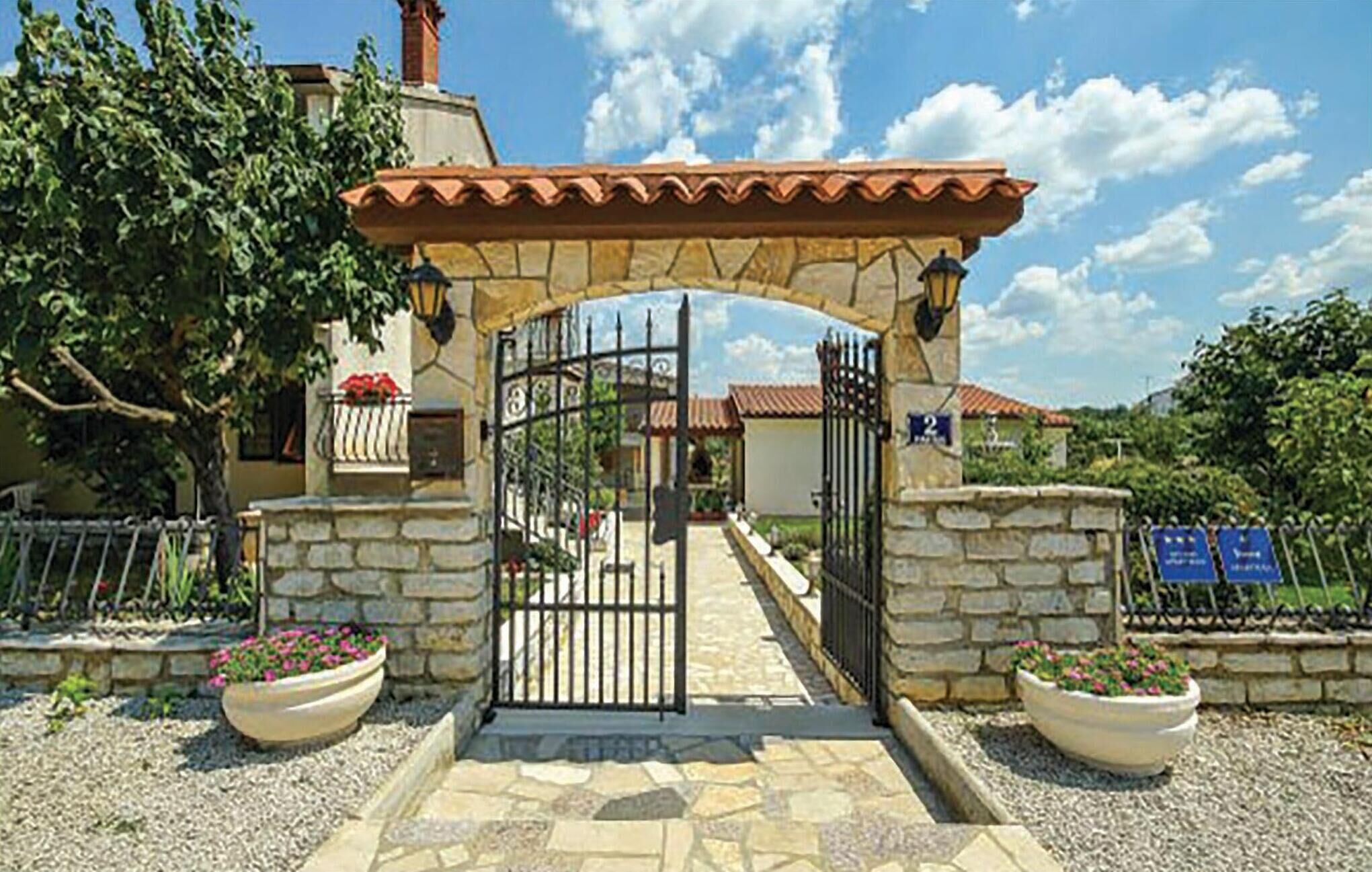 A gated entrance with a stone archway, a metal gate, and potted plants on either side.