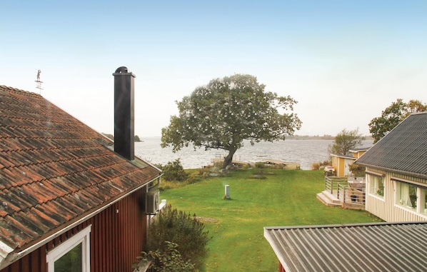 A residential area with a large tree in the yard, a body of water in the background, and a house with a sloped roof. - 2 bedroom awesome home in Sölvesborg (Sölvesborg)